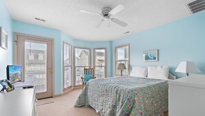 Ein Schlafzimmer mit Bett, Schreibtisch, Stuhl, Deckenventilator und einem Fenster mit Jalousien.