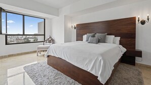 Een moderne slaapkamer met een groot bed, uitzicht op de stad en een bankje bij het raam.