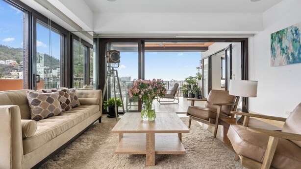 Een moderne woonkamer met een bank, stoelen, een salontafel en een stadsgezicht door grote ramen.