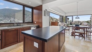 Een moderne keuken met een groot eiland, houten kastjes en een stadszicht door grote ramen.