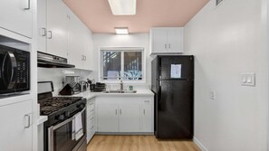 A compact kitchen with white cabinets, a black refrigerator, a stove, and a microwave. - The Pearl - Ocean Front (San Diego)