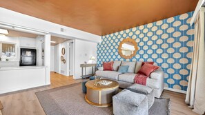 A modern living room with a sofa, coffee table, and patterned wallpaper. - The Pearl - Ocean Front (San Diego)