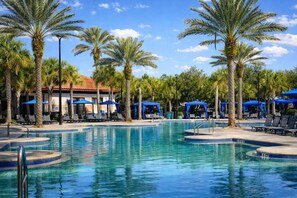 A swimming pool with lounge chairs and umbrellas, surrounded by palm trees and a building with a red roof. - Theater+Arcade Villa | 7BR Solterra | Near Disney (Davenport)