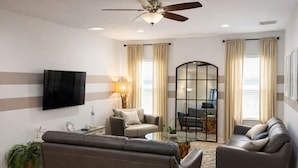 Ein Wohnzimmer mit Sofa, Sessel, Couchtisch, Fernseher und Deckenventilator.