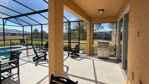 Ein überdachter Patio-Bereich mit Pool, Sitzgelegenheiten im Freien und einem Grill.