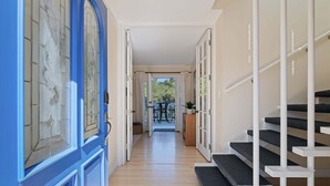 Corredor com porta azul, escada e vista para o exterior.
