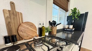 A kitchen with a gas stove, wooden cutting board, and various kitchen utensils. - Poolhouse Retreat / Outdoor Oasis & Pets Welcome (Yuma)