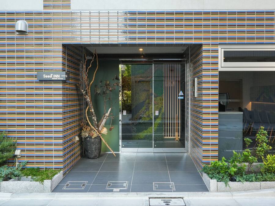 A modern building entrance with a striped facade, a sign for 'Seed Inn,' and a glass door leading inside.