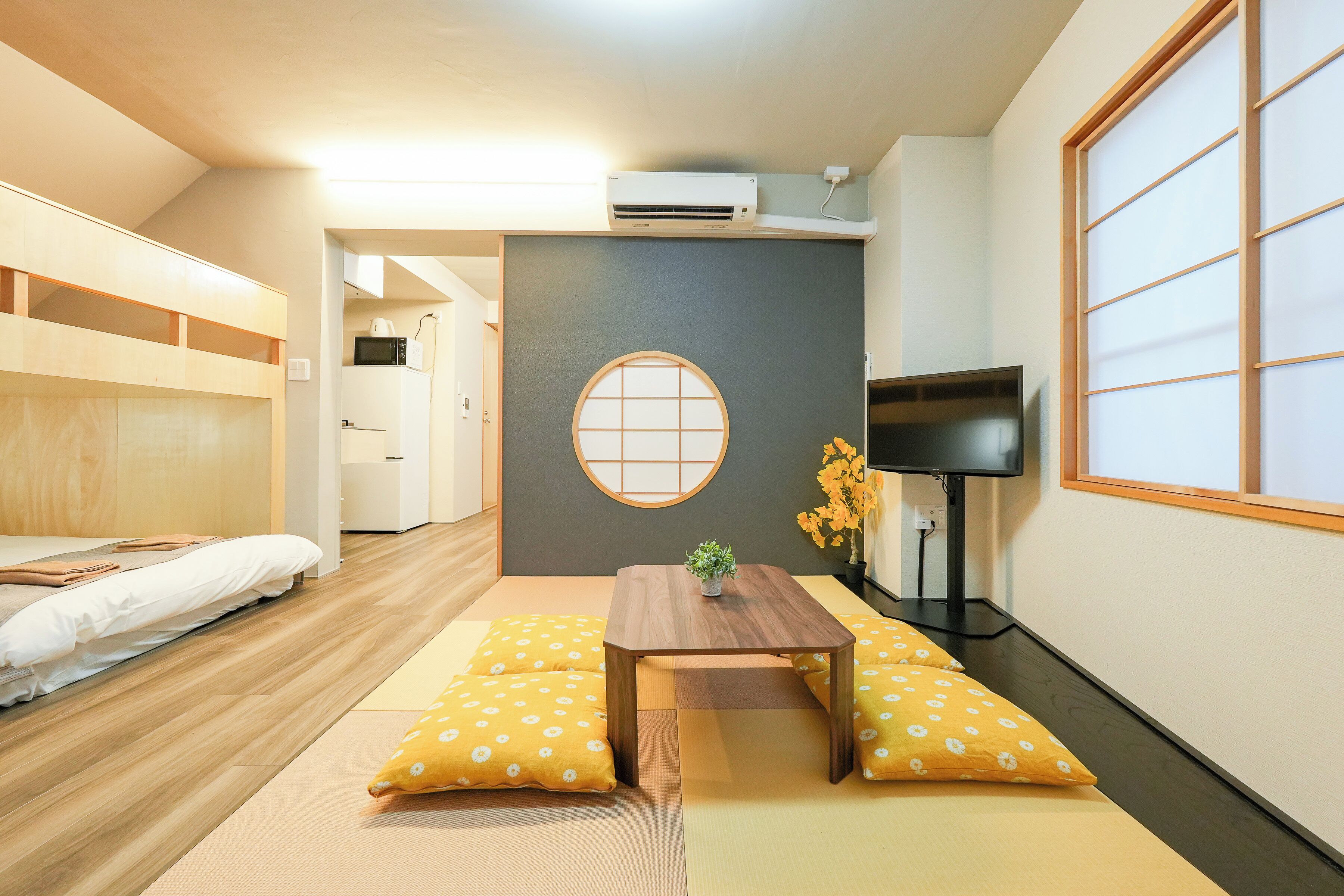 Una habitación con cama, una mesita con una planta, un televisor y una puerta corredera tradicional japonesa.