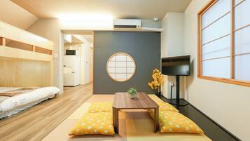 Una habitación con cama, una mesita con una planta, un televisor y una puerta corredera tradicional japonesa.