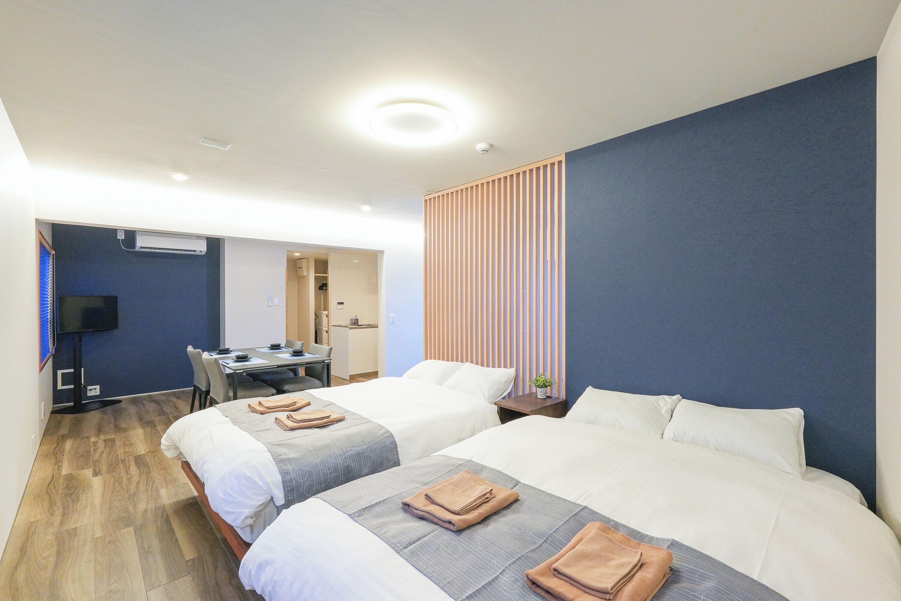 A hotel room with two beds, a desk, a chair, a TV, and a sliding door.