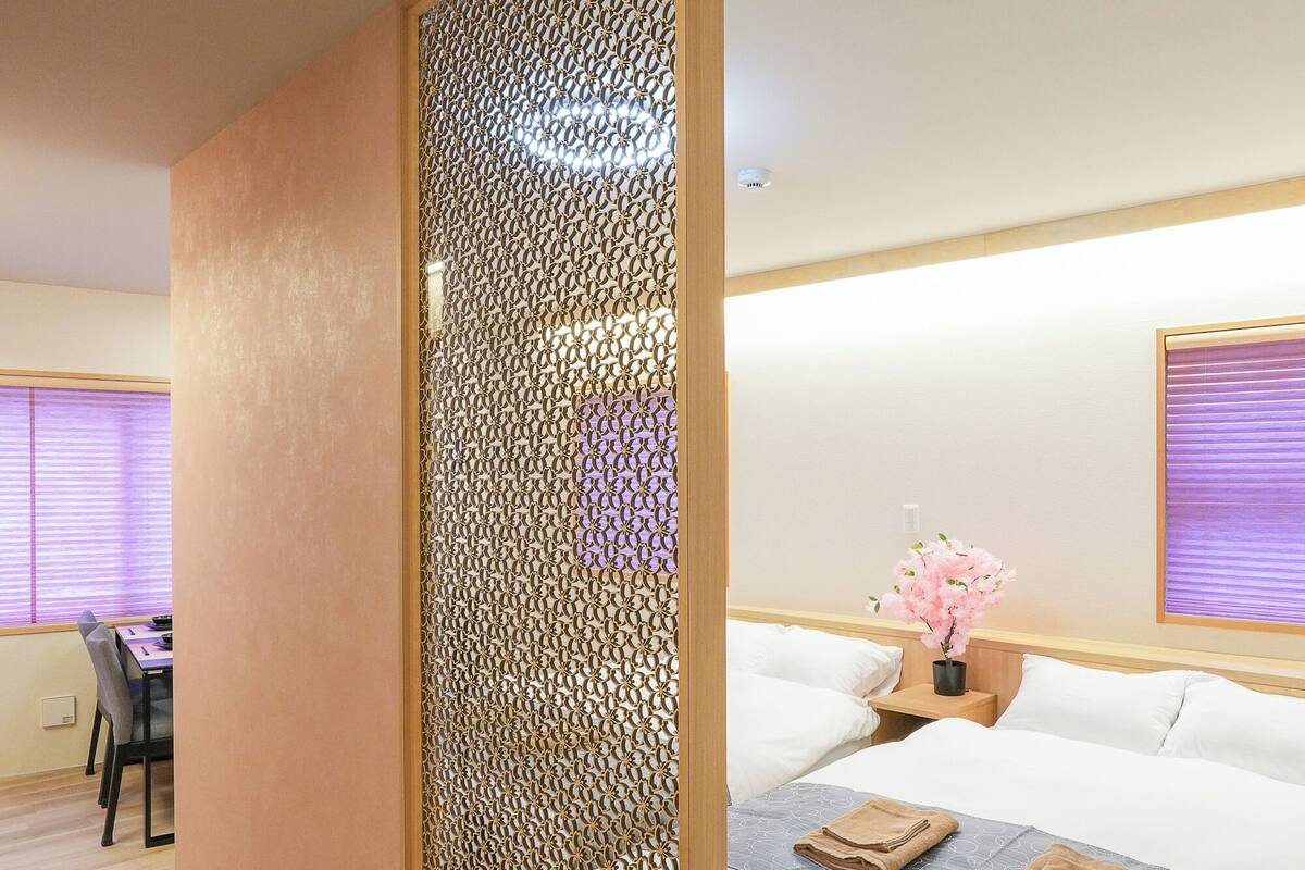 A hotel room with a bed, a desk, and a partition with a geometric pattern.