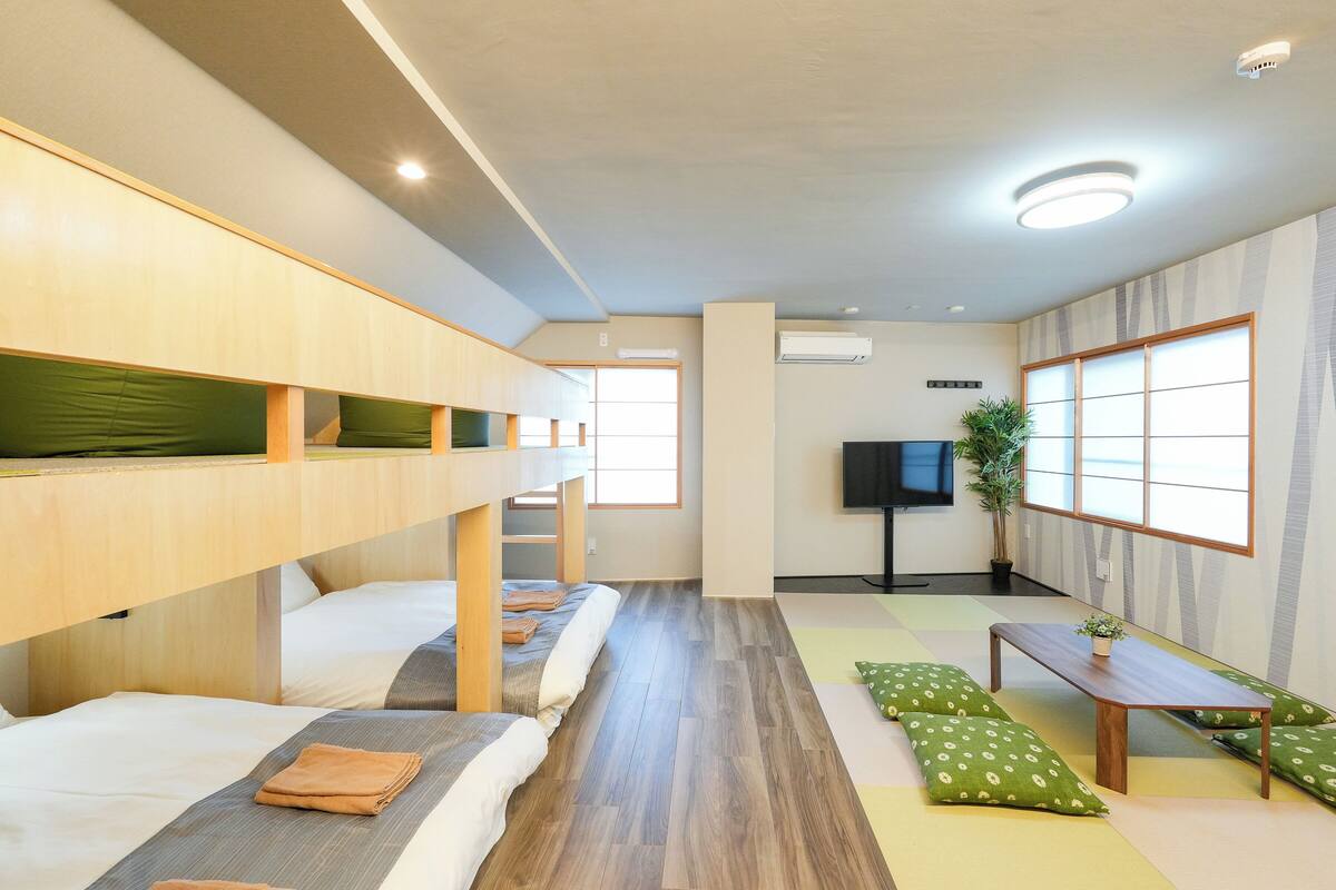 A room with bunk beds, a flat-screen TV, a small table, and a plant.