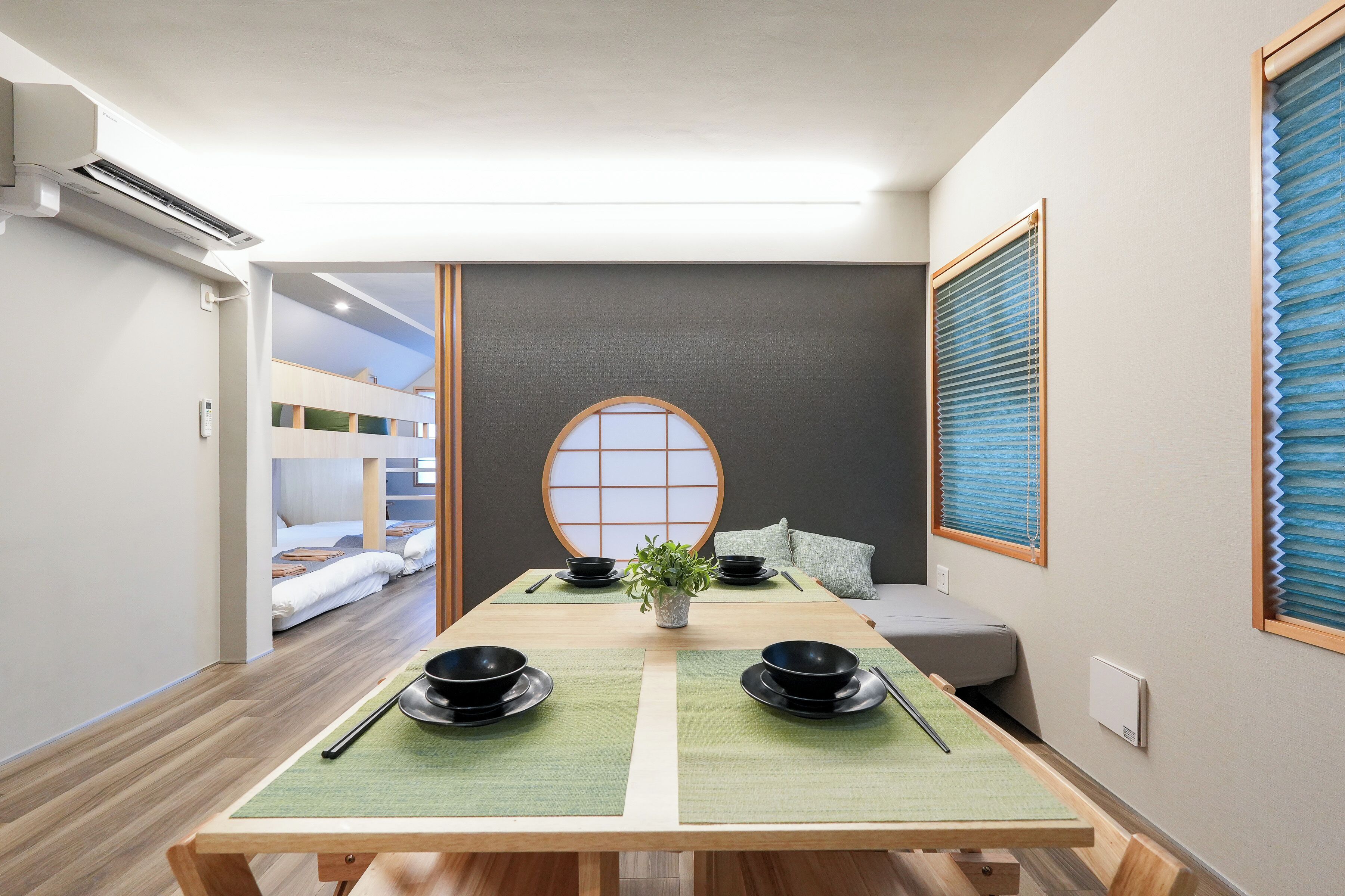 A room with a tatami mat table set for a meal, a futon bed, a shoji screen, and a bunk bed in the background.