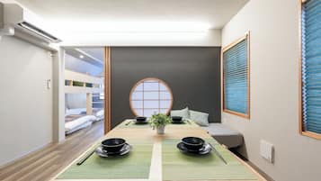 A room with a tatami mat table set for a meal, a futon bed, a shoji screen, and a bunk bed in the background.