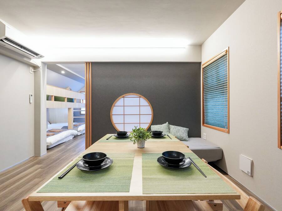 A room with a tatami mat table set for a meal, a futon bed, a shoji screen, and a bunk bed in the background.