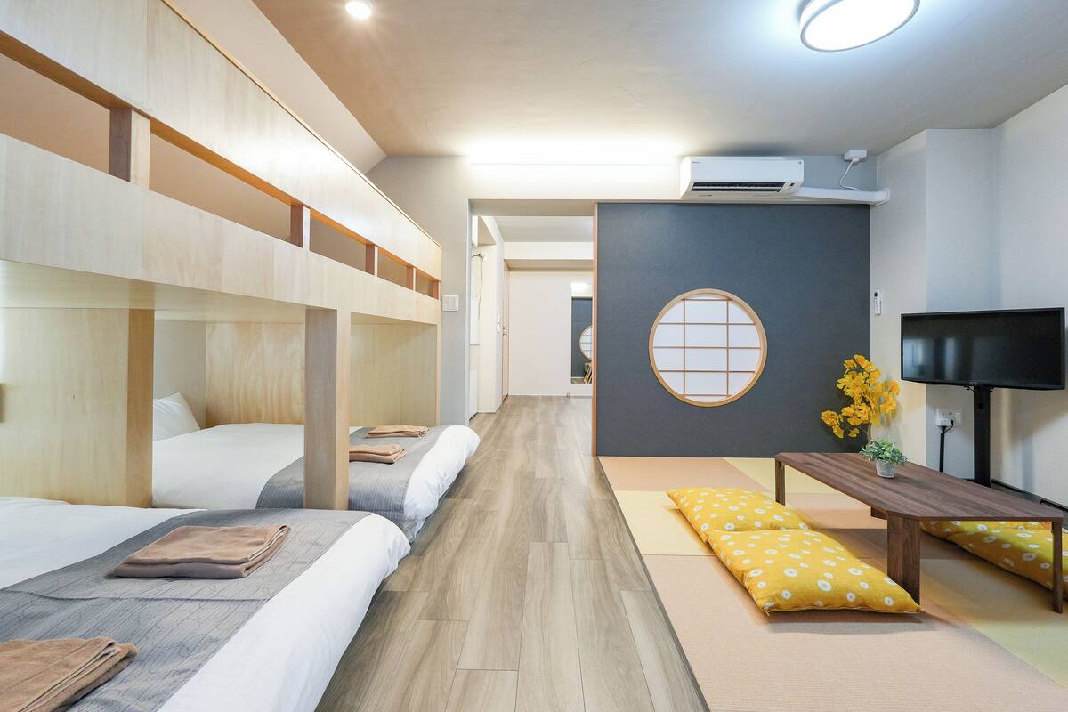A hotel room with bunk beds, a TV, a small table with a plant, and a tatami mat.