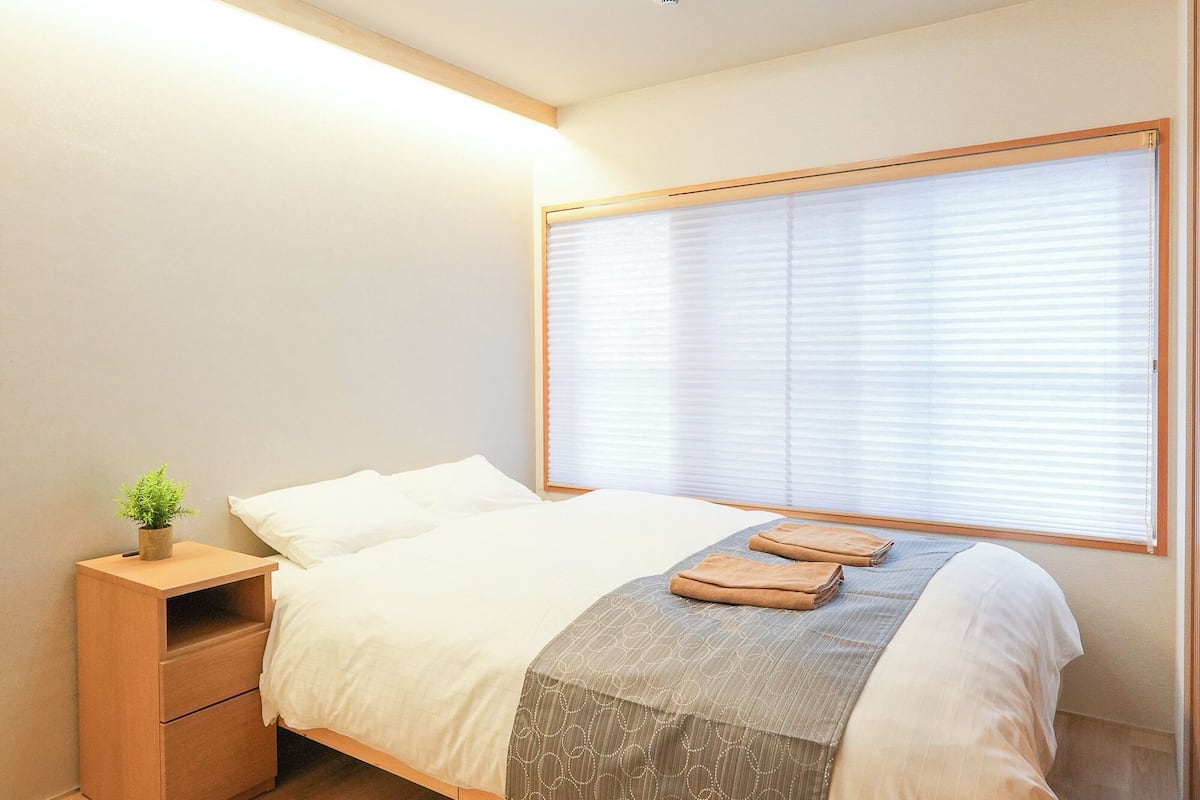 A bedroom with a bed, bedside table, and a window with blinds.