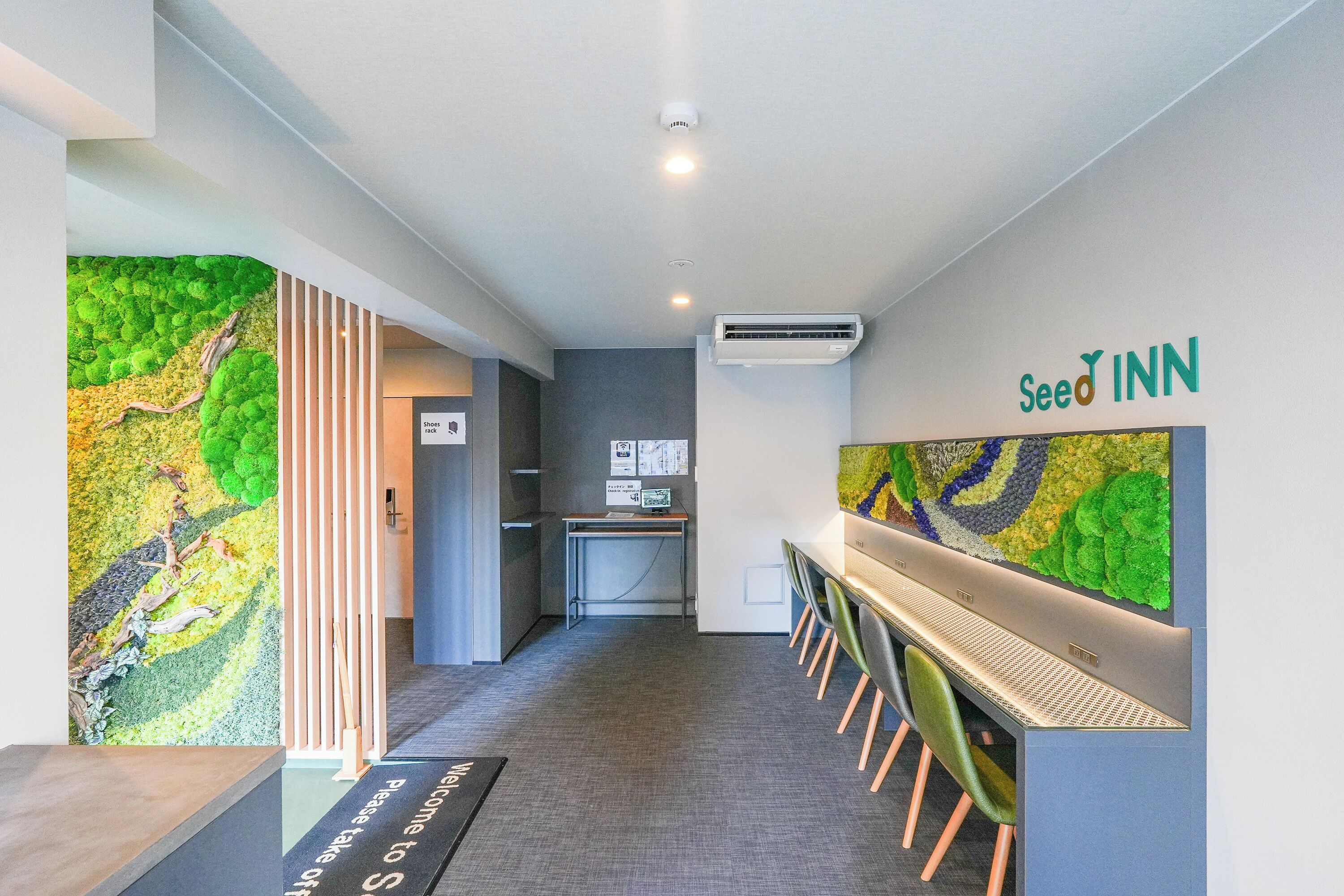 A hotel reception area with a green wall art, a reception desk, and a sign for 'Seed Inn'.