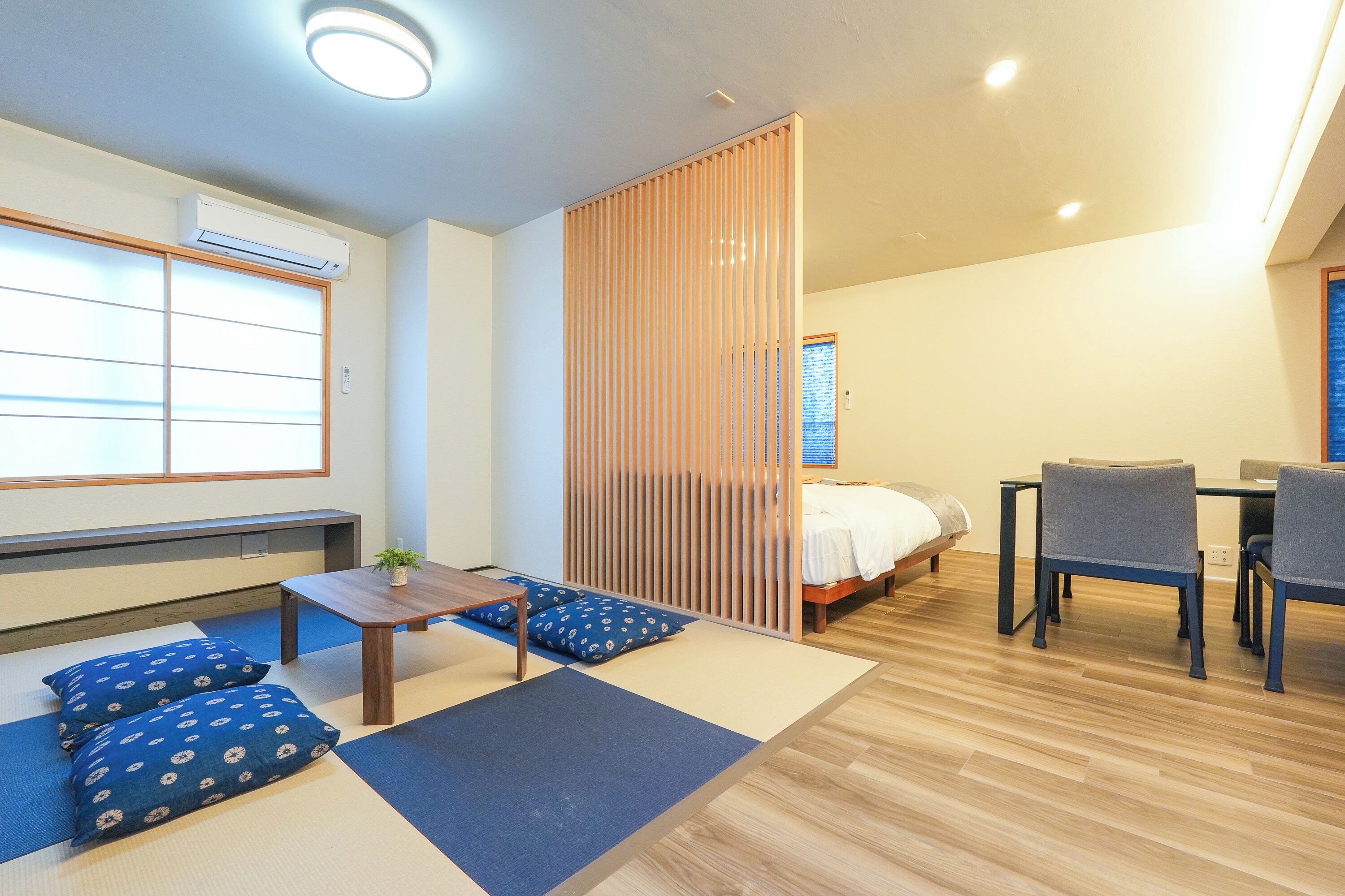A room with tatami mats, a bed, a desk, chairs, and a sliding door.