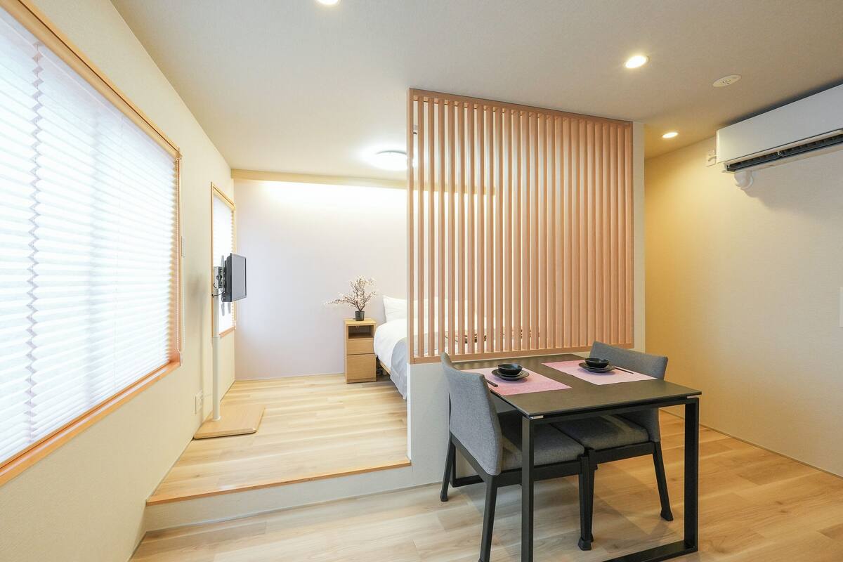A modern room with a dining table, chairs, a bed, and a sliding partition.