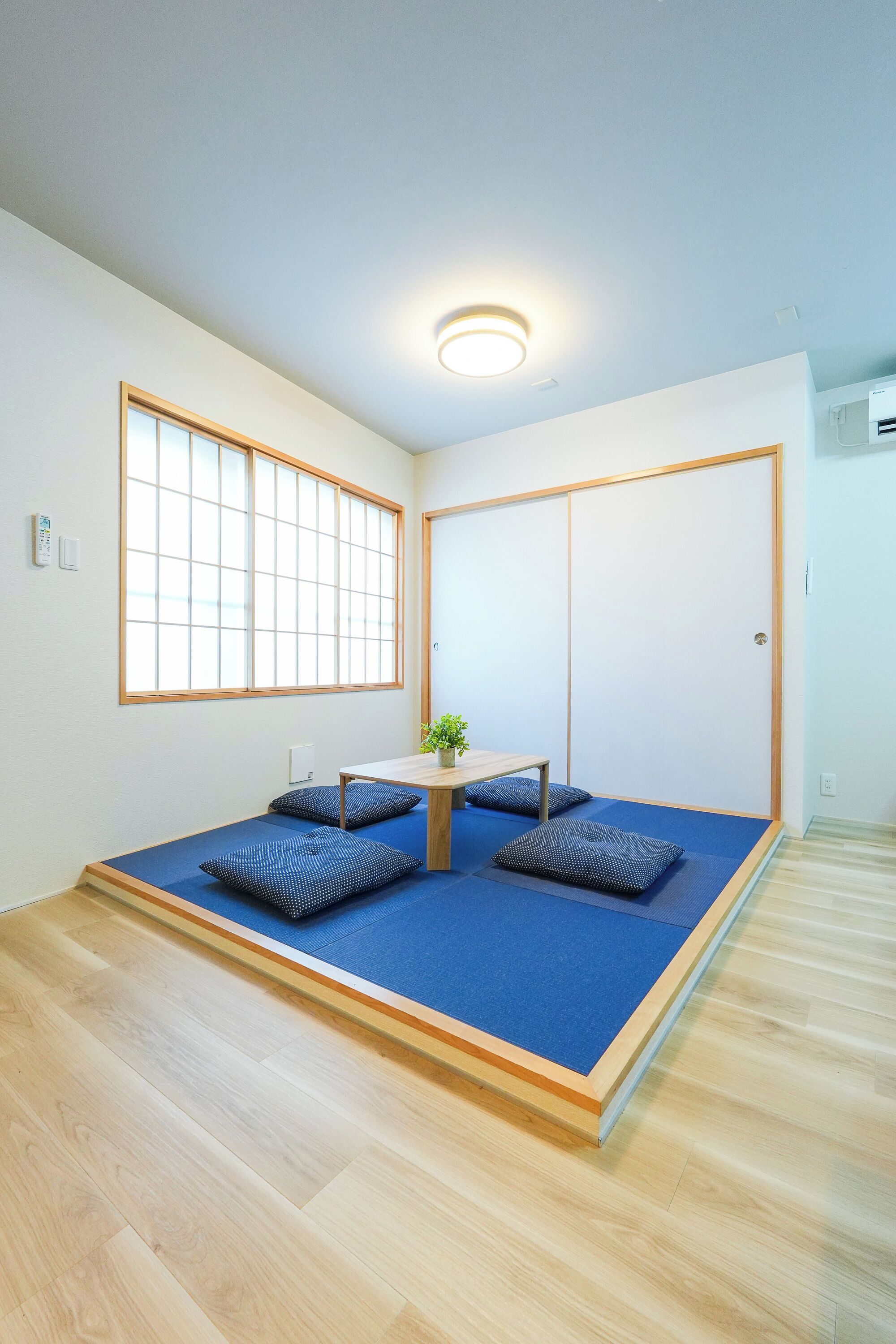 Una stanza con pavimento in tatami, un tavolino basso, due cuscini, una finestra con pannelli shoji e una porta scorrevole.