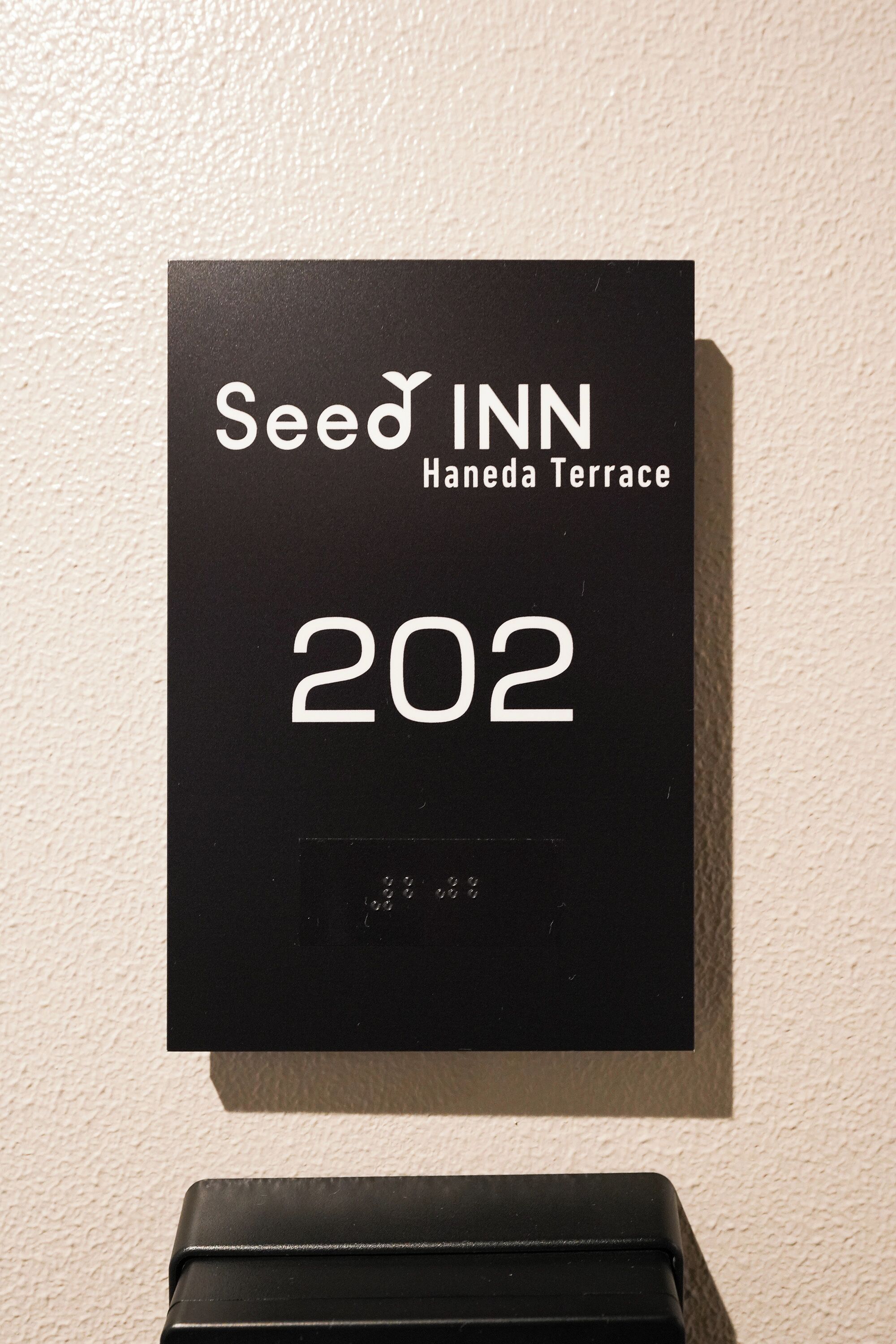 A black sign with white text for Seed Inn Haneda Terrace, room number 202.
