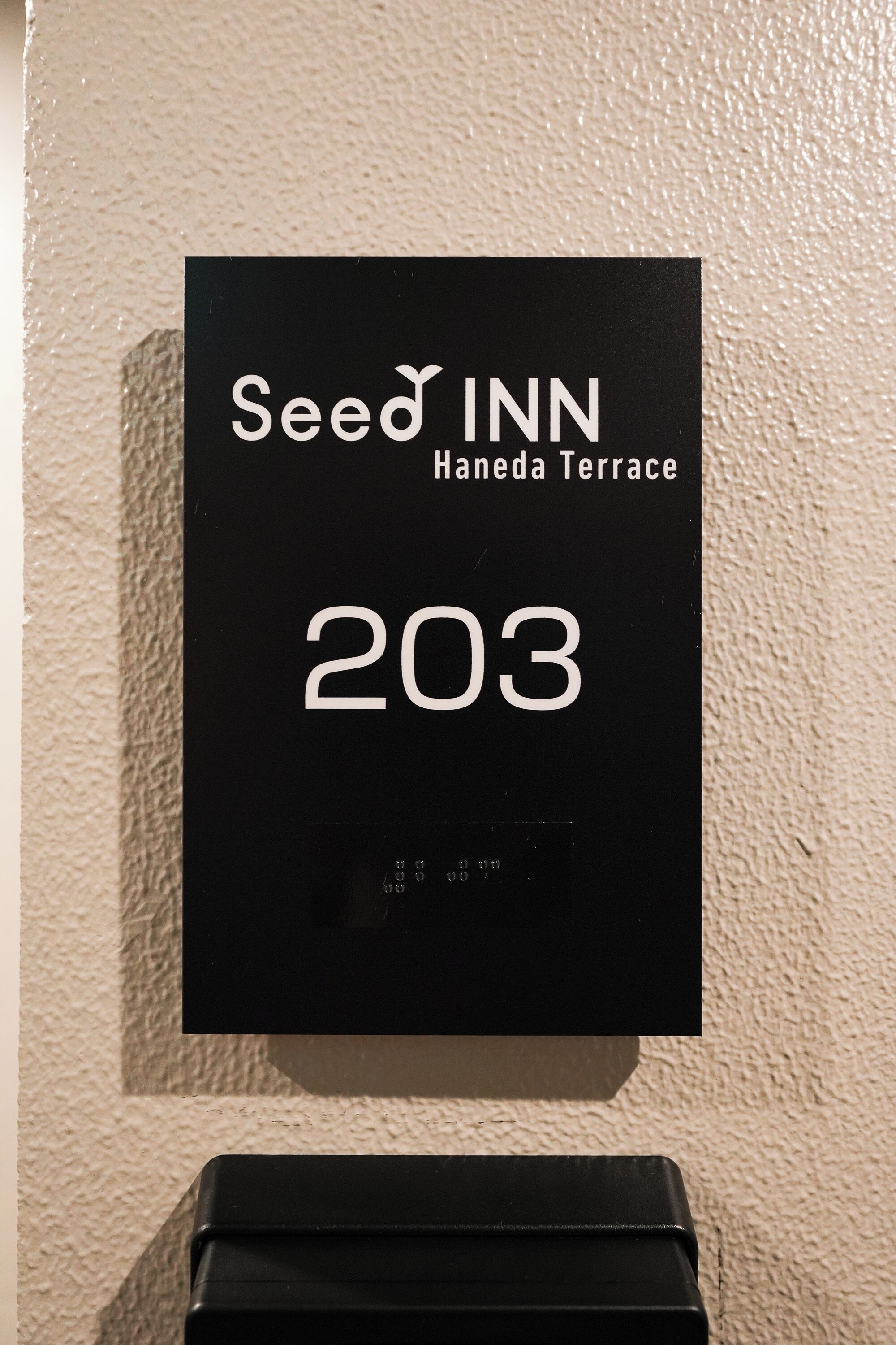 Placa preta com 'Seed Inn' e '203', indicando o nome do hotel e o número do quarto.