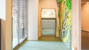 A hotel entrance with a welcome mat, a green wall with a tree design, and a glass door. - Seed INN Haneda Terrace (Tokyo)