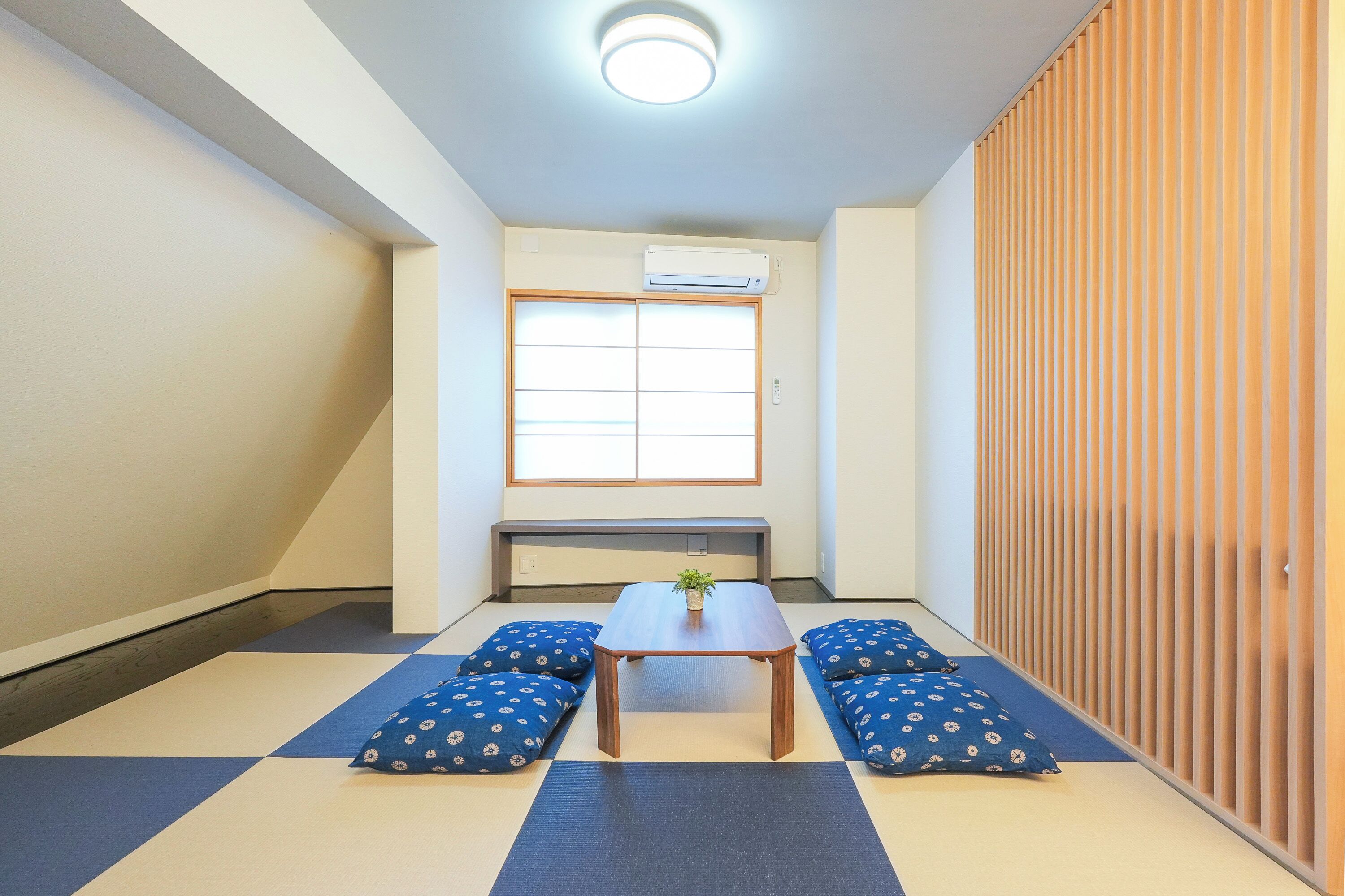 A room with tatami flooring, a low table with cushions, a window with blinds, and a sliding door.