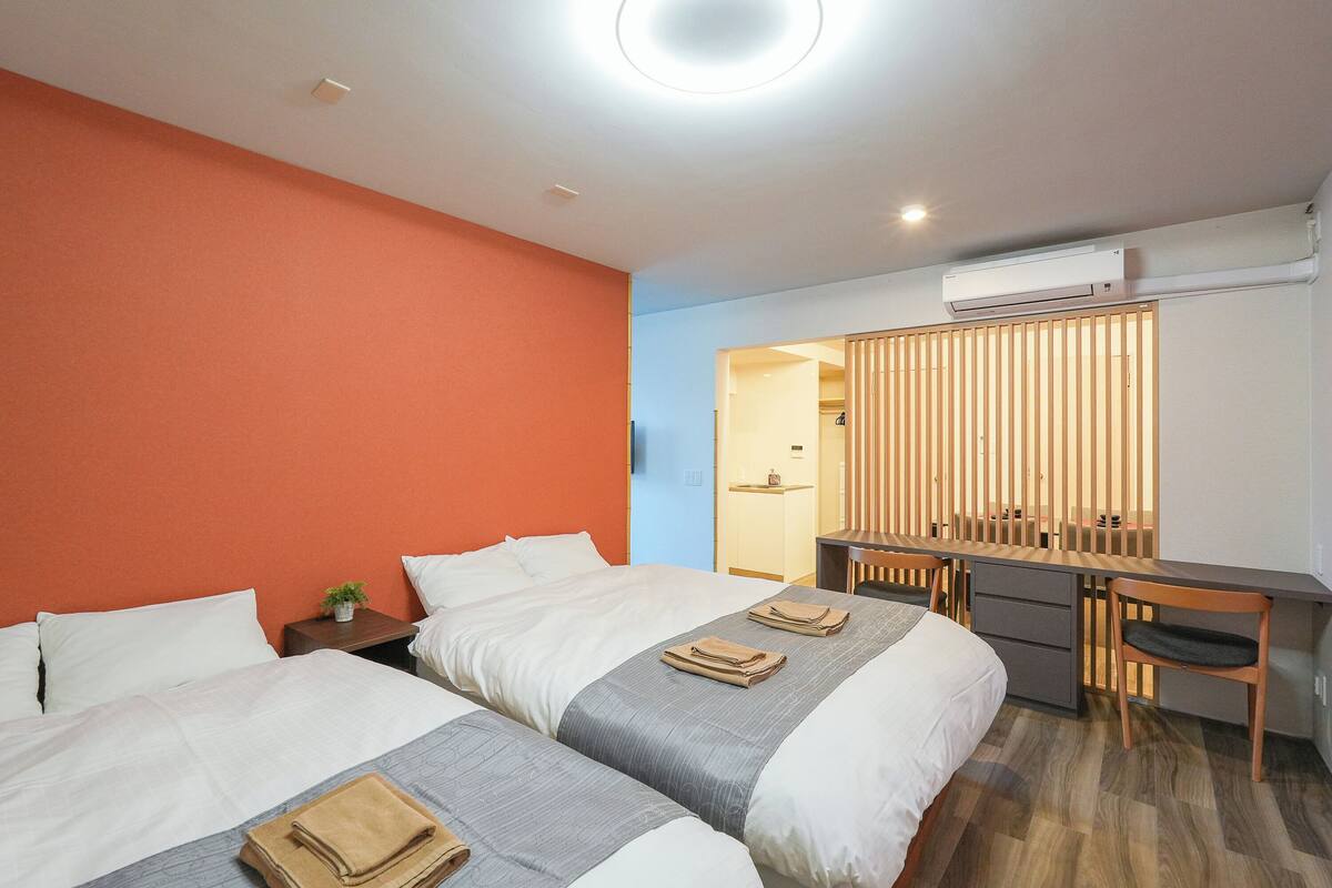 A hotel room with two beds, a desk, and an air conditioning unit.
