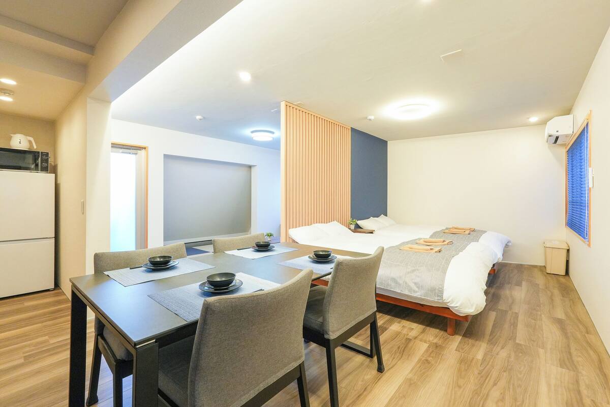 A modern hotel room with a dining area, a bed, and a kitchenette.