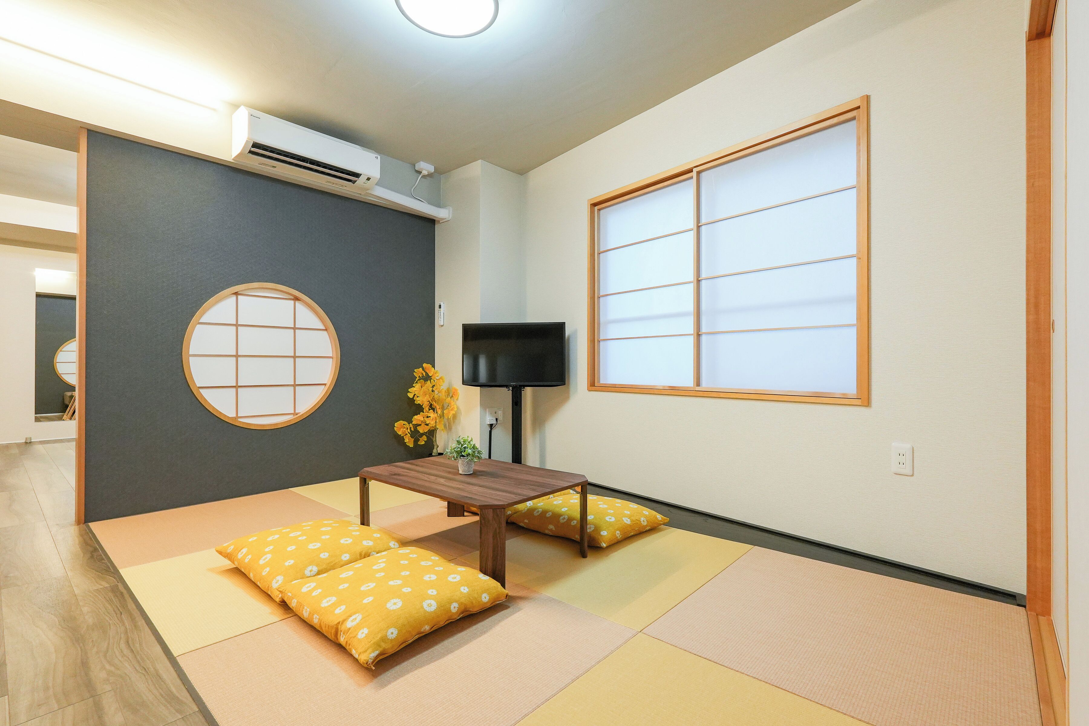 A room with tatami flooring, a television, a small table, and a window with a traditional design.