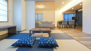 A modern living room with tatami mats, a low table, cushions, a sliding door, and a TV in the background. - Seed INN Haneda Terrace (Tokyo)