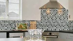Uma cozinha com ilha central, coifa de aço inoxidável e backsplash estampado.