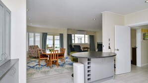 Cozinha moderna com ilha central, área de refeições com mesa e cadeiras, e vista pela janela.
