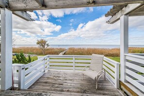 Une terrasse en bois avec une balustrade blanche, un banc et une vue sur la plage et l’océan.