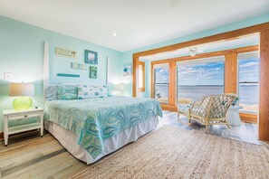Une chambre avec un lit, une table de chevet, une chaise et une vue sur l’océan.