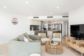 A modern living room with a sofa, chairs, a coffee table, and a TV. - Providence Oceanview Retreat with Pool & Spa (Caloundra Region)