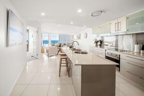 A modern kitchen with a central island, stainless steel appliances, and a view to the outside. - Providence Oceanview Retreat with Pool & Spa (Caloundra Region)