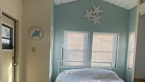 Un dormitorio con cama, ventilador de techo y dos ventanas con persianas.