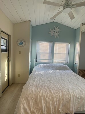 Ein Schlafzimmer mit einem Bett, einem Deckenventilator und zwei Fenstern mit Jalousien.
