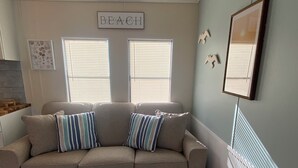 Una sala de estar con un sofá color crema, dos almohadas a rayas y un letrero con la palabra 'BEACH'.