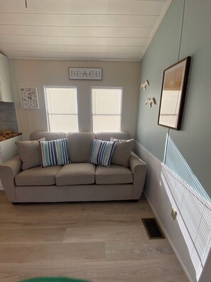 Ein Wohnzimmer mit einem beigefarbenen Sofa, zwei gestreiften Kissen und einem Schild mit der Aufschrift 'BEACH'.