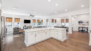 Een ruime keuken met witte kasten, een centraal eiland en een eethoek met tafel en stoelen.