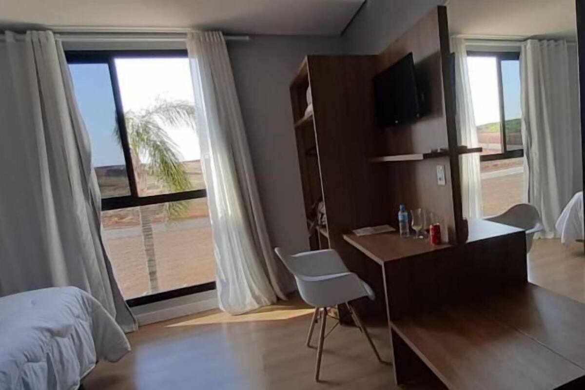 A hotel room with a bed, a desk, a chair, a TV, and a view of the desert landscape.