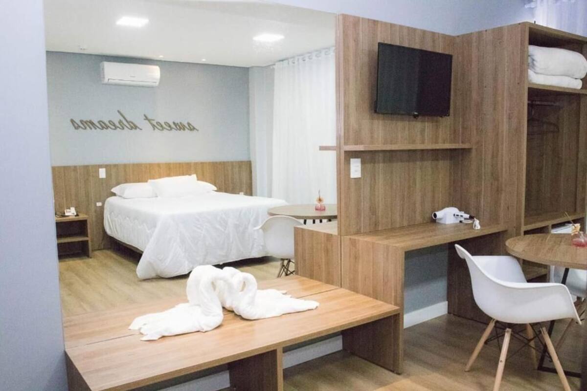 A modern hotel room with a bed, a desk, a chair, and a TV mounted on the wall.