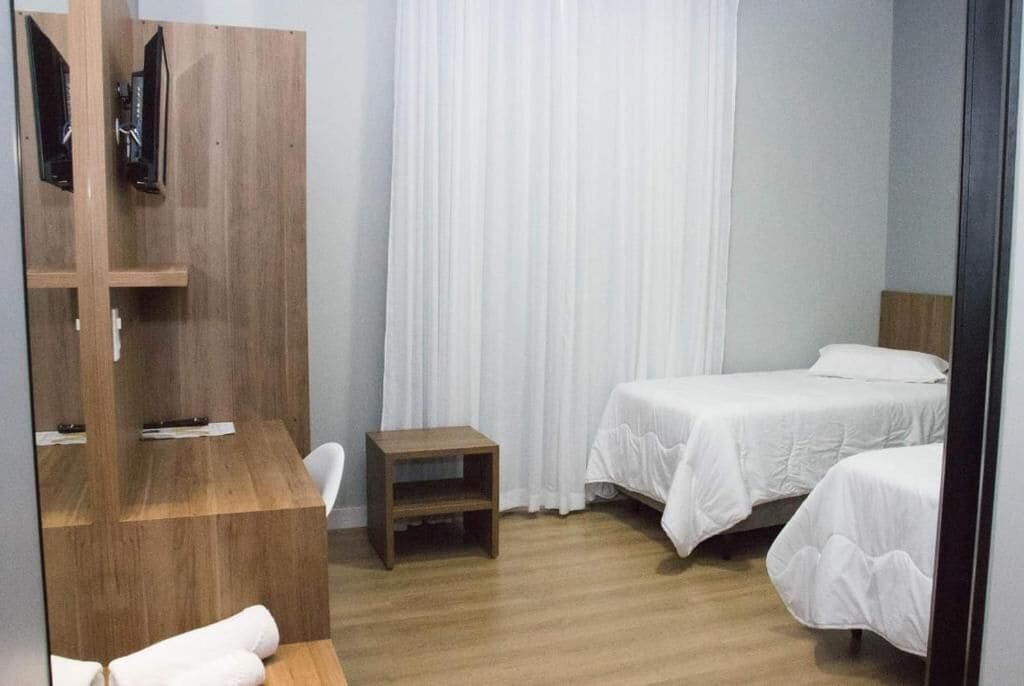 Un dormitorio con dos camas, un escritorio de madera, un televisor montado en la pared y una mesita.