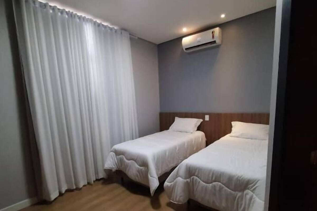 A hotel room with two single beds, a ceiling-mounted air conditioner, and wooden flooring.