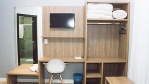 Une petite pièce comprenant un bureau en bois, une chaise, un téléviseur fixé au mur et une étagère avec des serviettes pliées.